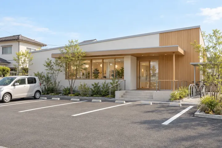 住宅地に建つ白い壁と木の平屋の歯科医院と、前の駐車場(AIで作成した見本写真)